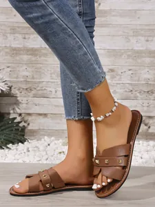 Close-up van bruine platte sandalen met gouden studs aan de voeten van een model.