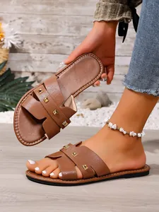 Bruine platte slippers met piramide-studs en H-vormig bandontwerp.