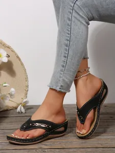 Detailed view of black platform flip-flop sandals with gold metal chain decoration.
