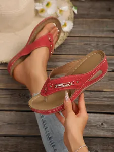 Detailed view of red wedge flip-flop sandals with elegant metal chain decoration