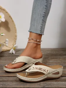 Close-up of women's beige wedge flip-flops with decorative metallic chain and rhinestones