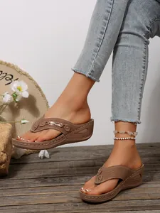 Close-up detail of women's brown wedge thong sandals with metal chain decor