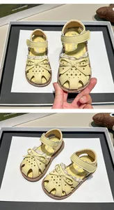 Close-up detail of yellow children's closed-toe sandals with bow and lace trim
