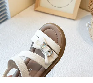 Close-up of girl's princess sandal featuring a white leather bow and sparkling rhinestones.