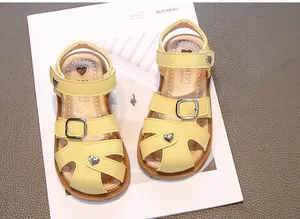 Detail of yellow girls' sandals with heart-shaped buckle and soft anti-slip sole.