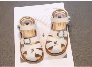 Close-up view of white girls' closed-toe sandals with heart accents and buckle strap