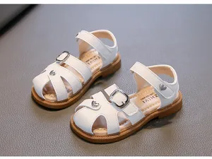 Close-up view of white girls' sandals featuring silver heart charms and buckle straps
