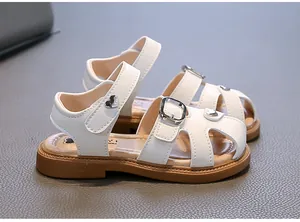 Detail view of white girls' sandals with heart-shaped buckle and soft brown sole.