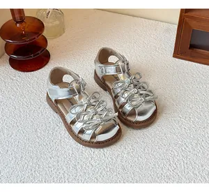 Side view of silver metallic girls sandals featuring triple bow accents and brown soles