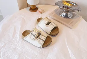 Detailansicht cremefarbener Kindersandalen mit Fransen und Doppelschnallen auf Papier.