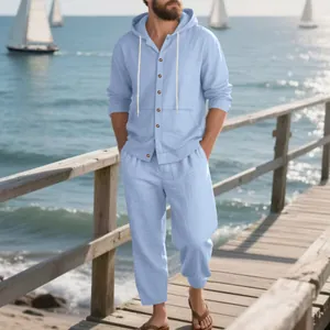 Hombre con un conjunto de lino azul claro y capucha en un pintoresco muelle de madera