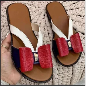 Detail of flat sandals featuring a red bow and white and navy straps.