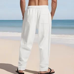Men's loose white linen pants shown from the back in a scenic sunny beach setting