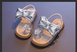 Elegant silver girl's sandals featuring metallic bow and rhinestone flower detail macro view