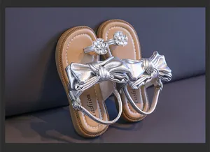 Close-up detail of girls' silver metallic princess sandals featuring large bows and rhinestones.