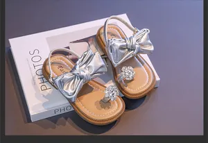 Detailed view of silver girls' sandals featuring bow and rhinestone flower ornaments