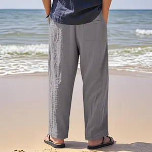 Back view of grey linen loose straight casual trousers for men shown in a beach setting