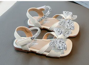 Détail en gros plan du nœud en strass et de la bride sur les sandales crème pour enfants
