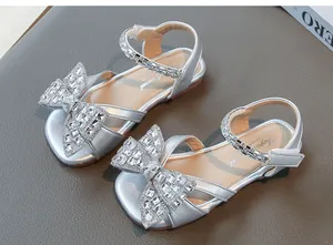 Gros plan de sandales argentées fille avec grands nœuds en strass et brides pailletées.