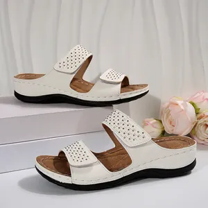 Gros plan sur les sandales compensées blanches avec brides velcro ornées de strass