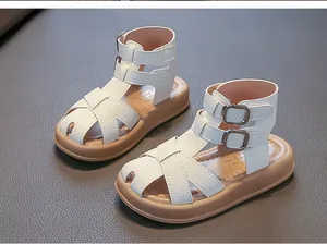 Detailansicht weißer geflochtener Römersandalen für Mädchen mit weichen braunen Sohlen.