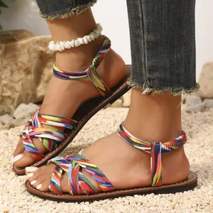Detailansicht von ethnischen flachen Sandalen mit bunten Webriemen auf einem Kieshintergrund