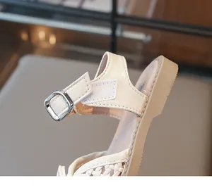 Close-up view of a cream woven girl's sandal featuring an adjustable strap and soft sole