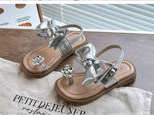 Detail view of girls' silver metallic sandals with large bow and rhinestone flower