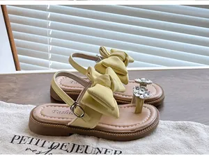 Detail of girl's yellow sandals with large bow-knot and rhinestone flower embellishment