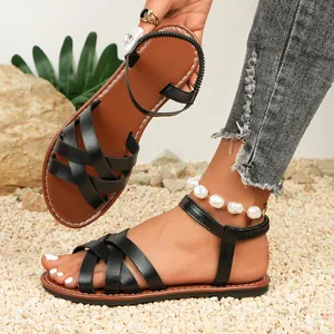 Close-up of black strappy flat sandals with elastic back strap on a pebble beach
