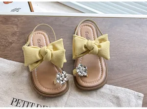 Close-up of stylish yellow girl's sandals with large bow and rhinestone flower detail