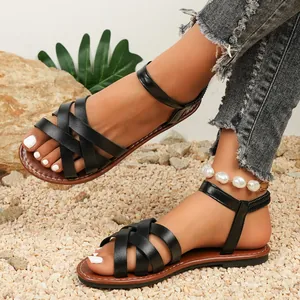 Close-up detail of women's black crossover strap flat sandals on outdoor gravel ground