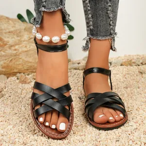 Close-up of stylish black Roman flat sandals with cross straps and ankle buckle on gravel