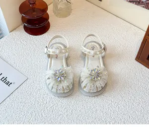 Nahaufnahme von weißen Mädchen-Prinzessin-Sandalen mit Strassblumen und Perlenriemen