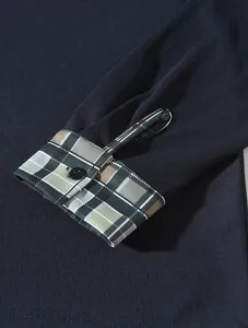 Detailansicht eines dunkelblauen Poloshirts mit karierten Manschetten und schwarzem Knopf.