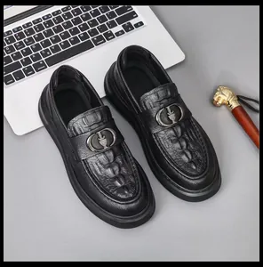 Detail view of black crocodile-embossed leather loafers with a crown metal buckle.