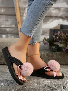 Close-up of women's black platform flip-flops with pink fur pom-poms on stone steps.