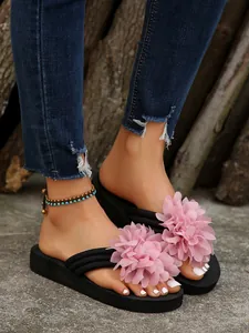 Close-up detail of stylish black flip flops featuring large pink fabric flowers and platform sole