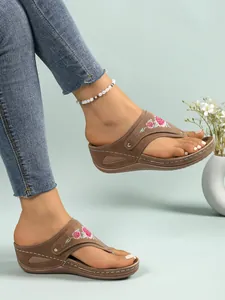 Brown platform thong sandals with floral embroidery shown on feet in lifestyle setting