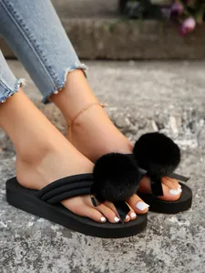 Close-up detail of black platform thong sandals with fluffy fur pom-poms and satin bows