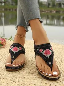 Detail shot of black thong sandals featuring vibrant rose floral embroidery on straps.