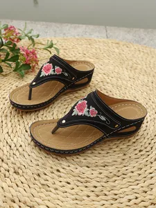 Detailed view of black wedge flip-flops with elegant floral embroidery and platform soles