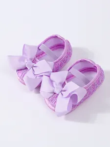 Detailaufnahme lilafarbener Babyschuhe mit großer Schleife und atmungsaktiver Spitze