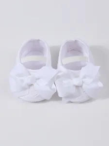 Detailansicht weißer Baby-Spitzenschuhe aus Spitze mit großen Ripsband-Schleifen