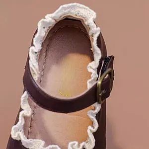 Nahaufnahme brauner Baby-Mädchen-Schuh mit weißer Spitze und Metallschnalle