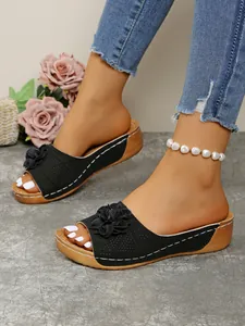 Detail of black wedge slide sandals featuring an elegant 3D flower and stylish contrast stitching.