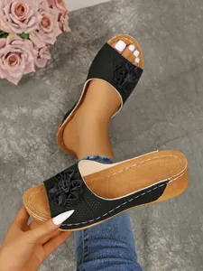 Detail of women's black wedge sandals with 3D floral accent and contrast stitching.