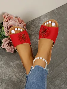 Close-up of red flower wedge slide sandals on feet with stylish white pedicure for summer