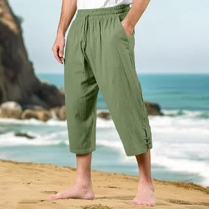 Detailed view of men's casual linen beach pants in sage green on a sunny shore