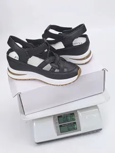 Black wedge sandals with woven straps and velcro closure shown on weighing scale